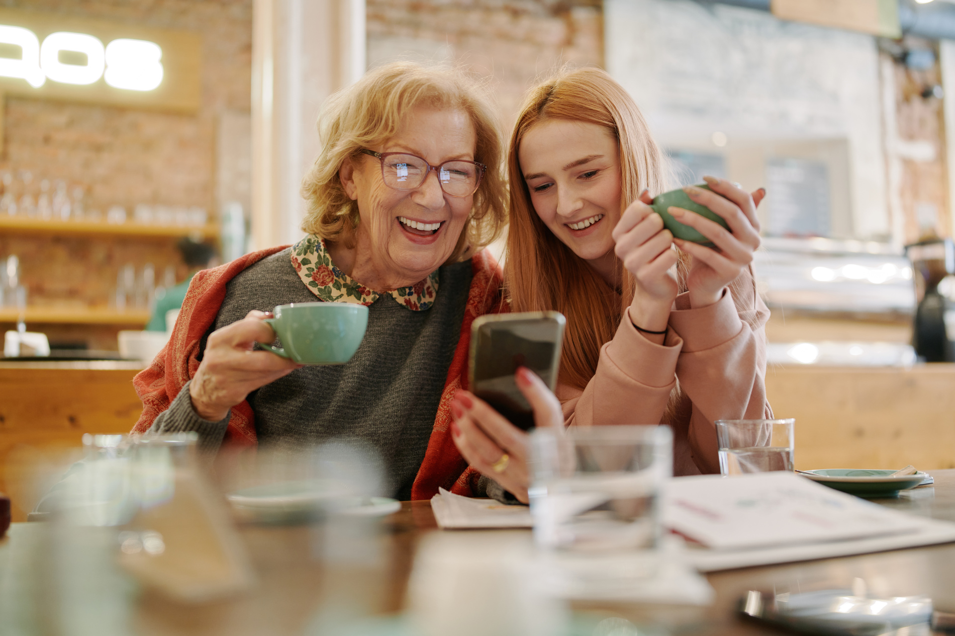 Une grand-mère heureuse et sa petite-fille adolescente dégustant un café.